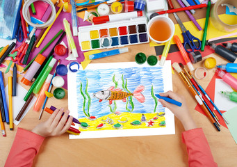 Naklejka premium child drawing fish underwater and seabed, top view hands with pencil painting picture on paper, artwork workplace