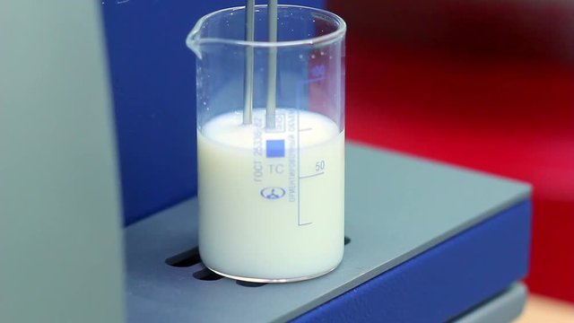 Biologist put measuring cup with a liquid in laboratory equipment. Closeup. Scientist put glas with milk in laboratory equipment for test. Quality test. Quality control at dairy factory