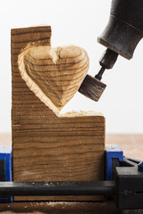 Sanding wood in heart shape with a rotary tool, on white