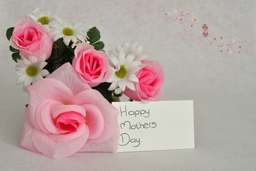 A bunch of artificial flowers with a card for happy mothers day isolated on a white background