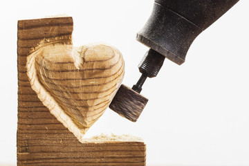 Sanding wood in heart shape with a rotary tool, on white, horizontal