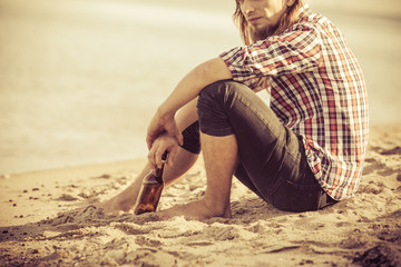 Man depressed with wine bottle sitting on beach outdoor