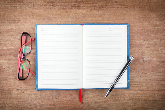 Blank open notebook with pen and glasses on wood table,Business