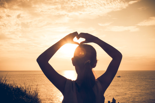Silhouette woman hands in shape of love heart  at sunset.