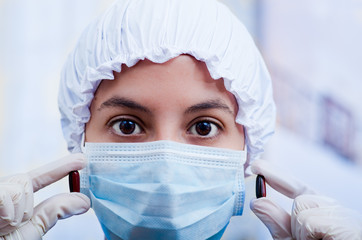 Closeup headshot nurse wearing bouffant cap and facial mask holding up two pill capsules for camera