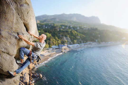 Side view of young man rock climber making difficult move up on multi-pitch against scenic sea coast background. Climbing equipment. Healthy lifestyle concept. Panoramic picture