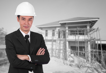 engineer in helmet with arms crossed, house construction backgro