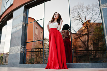 Portrait of fashionable girl at red evening dress posed backgrou