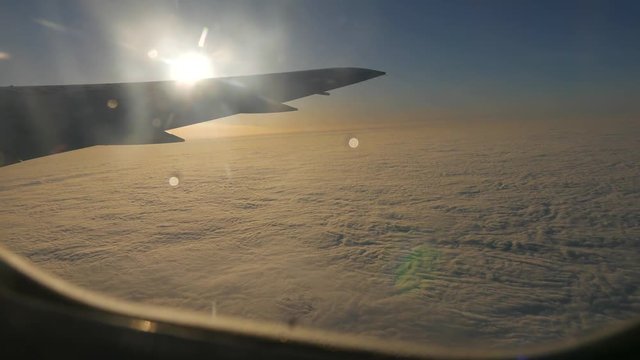 View from the illuminator of a plane flying over the cloud cover. View to wing, blue sky and the sun before sunset