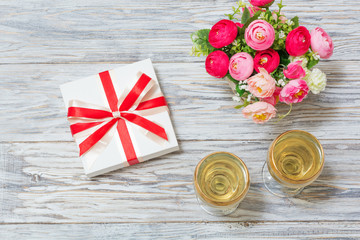Two glasses of white wine, flowers and a gift