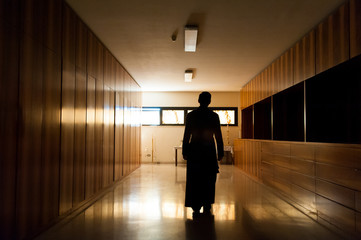 Shadow of young priest dressed in black walking alone in dark moody church
