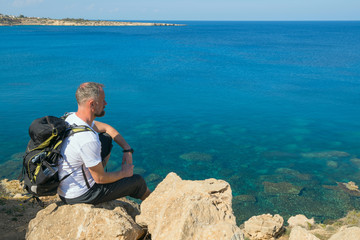 Backpacker sitting on the rocky shore transparent sea