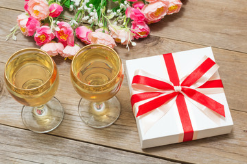Two glasses of white wine, flowers and a gift