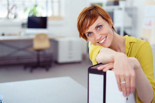 lächelnde mitarbeiterin im büro stützt ihren kopf auf aktenordner