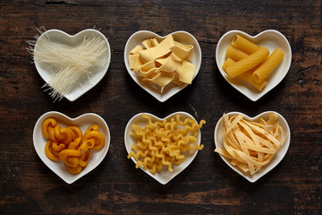Six types of uncooked pasta in heart shaped bowls