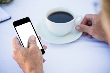Close up of masculine hands using smartphone and having coffee on a table