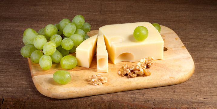 Cheese with brush of grapes and walnuts on a wooden table