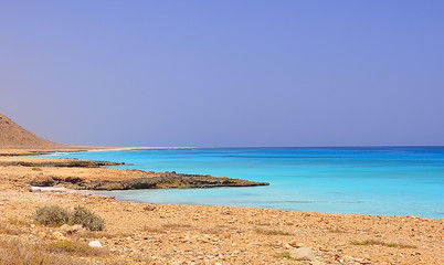Fototapeta na wymiar sandy desert lifeless rocky shore of the Aral Sea on the island of Socotra, Yemen. Turquoise amazing color clean water into the sea. Bright blue sky on a sunny hot day. 