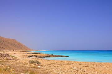 sandy desert lifeless rocky shore coastline of the Aral Sea. Mountain , cliffs descend to the water on the horizon. Socotra, Yemen. Turquoise amazing color clean water into the sea. sunny  day.
