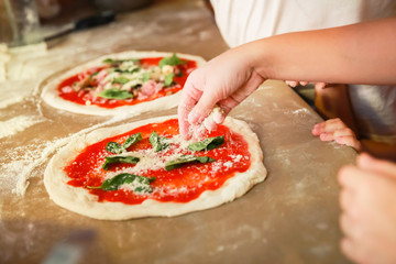 Preparing Pizza Margherita, cook adds cheese