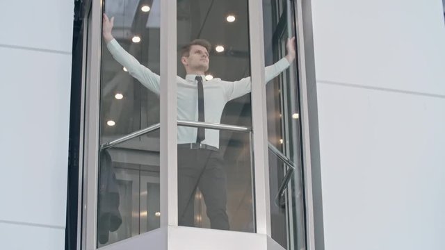 Young businessman standing in the moving up glass elevator and looking at the business center