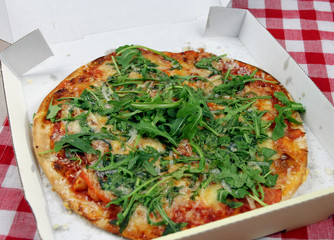Vegetarische Pizza mit Rucola, Tomaten und Parmesan im Pappkarton