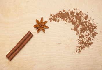 Obraz na płótnie Canvas Magic wand made of cinnamon stick, star anise and cocoa powder on wooden background. Magic aromatic spices for healthy and flavored food.