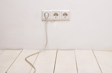 Three white electrical outlets with white power cord and plug on white wall.