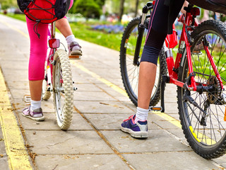 Naklejka premium Bikes bicyclist girl. Children feet and bicycle wheel. Low section. Girls children cycling on yellow bike lane. Bike share program save money and time at city street. 