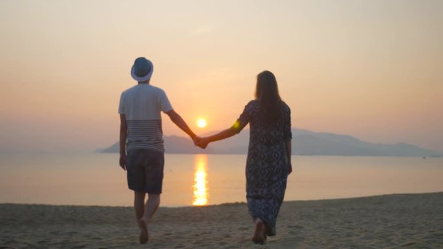 Romantic couple expexting baby walking on a sea shore holding hands and kissing on sunset background. Shallow focus