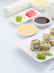 Japanese cuisine. Shrimp sushi roll ith sauces ginger and wasabi on a hite plate.