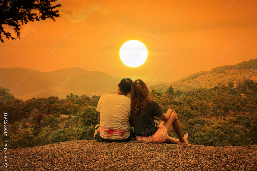 Wall mural Romantic of couple love sitting on the stone looking sunset at m