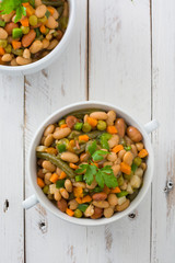 White beans with vegetables on white wooden table
