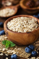 Rolled oats in a wooden bowl with fresh blueberries, sprig of mint and honey at the background. Shallow depth of field