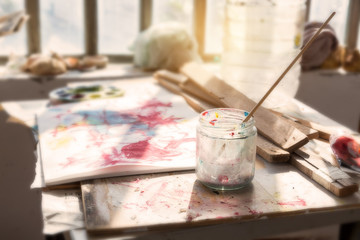 Thin paintbrush in a glass jar and palette in art workshop.