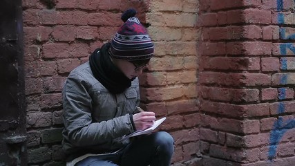 Romantic young man sitting alone in deserted place, writing poetry in notepad