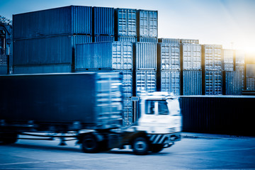  stacked containers and passing truck at harbor,blue toned image.