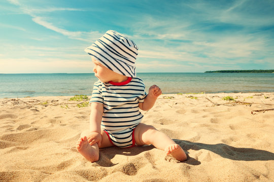 Little Baby Boy Sitting On The Beach In Summer Day