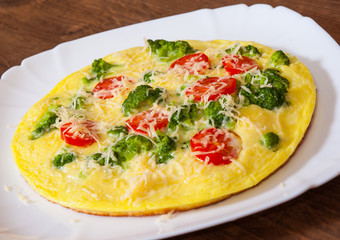 omelet with tomato, broccoli and cheese in a plate on wooden table