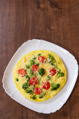 omelet with tomato, broccoli and cheese in a plate on wooden table
