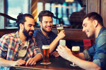 male friends with smartphone drinking beer at bar