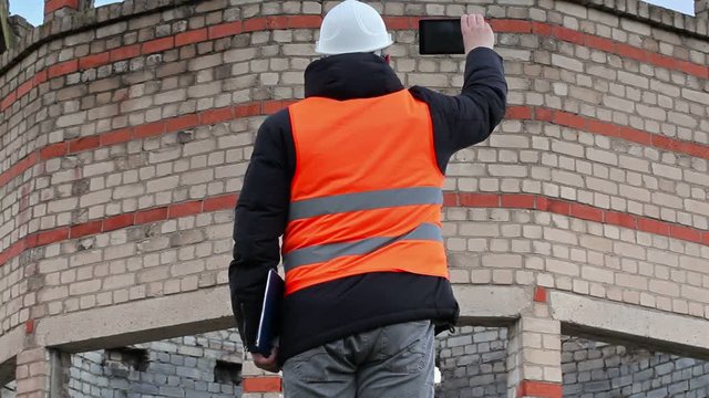 Civil engineer take pictures on tablet PC near building 
