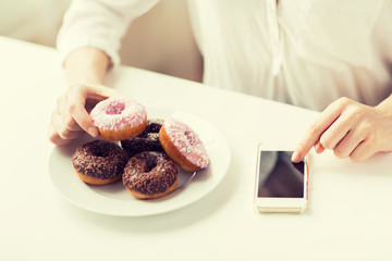 close up of hands with smart phone and donuts