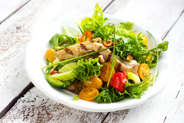 Delicious salad with grilled chicken breast on a wooden background
