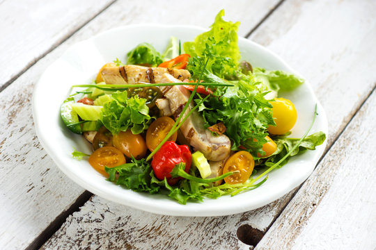 Delicious salad with grilled chicken breast on a wooden background