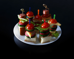 Small snacks canape with cherry tomatoes, cheeze, sausages and vegetables on bread on skewers on white plate