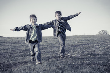 Two boys running together on meadow, sepia toned