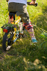 Close up of little kid boy riding on his bicycle  with flowers, outdoors. Boy riding his first yellow bike on a meadow. Leisure activities for children outdoors. Summer time. Happy summer concept