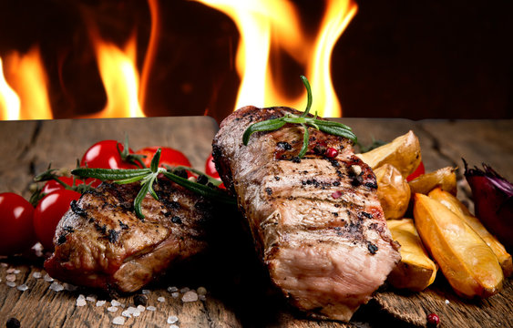 Delicious beef steakes on wood with fire background