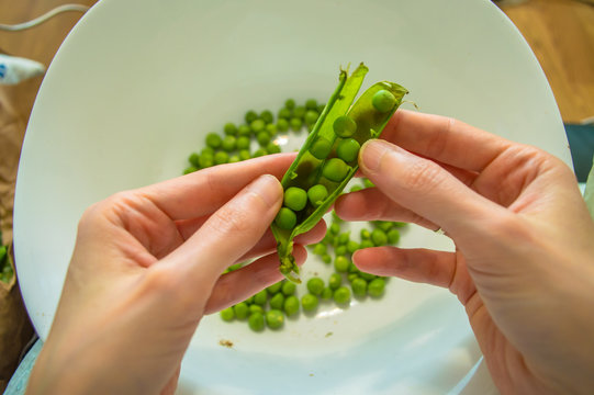 Woman podding fresh green peas in a white bowl